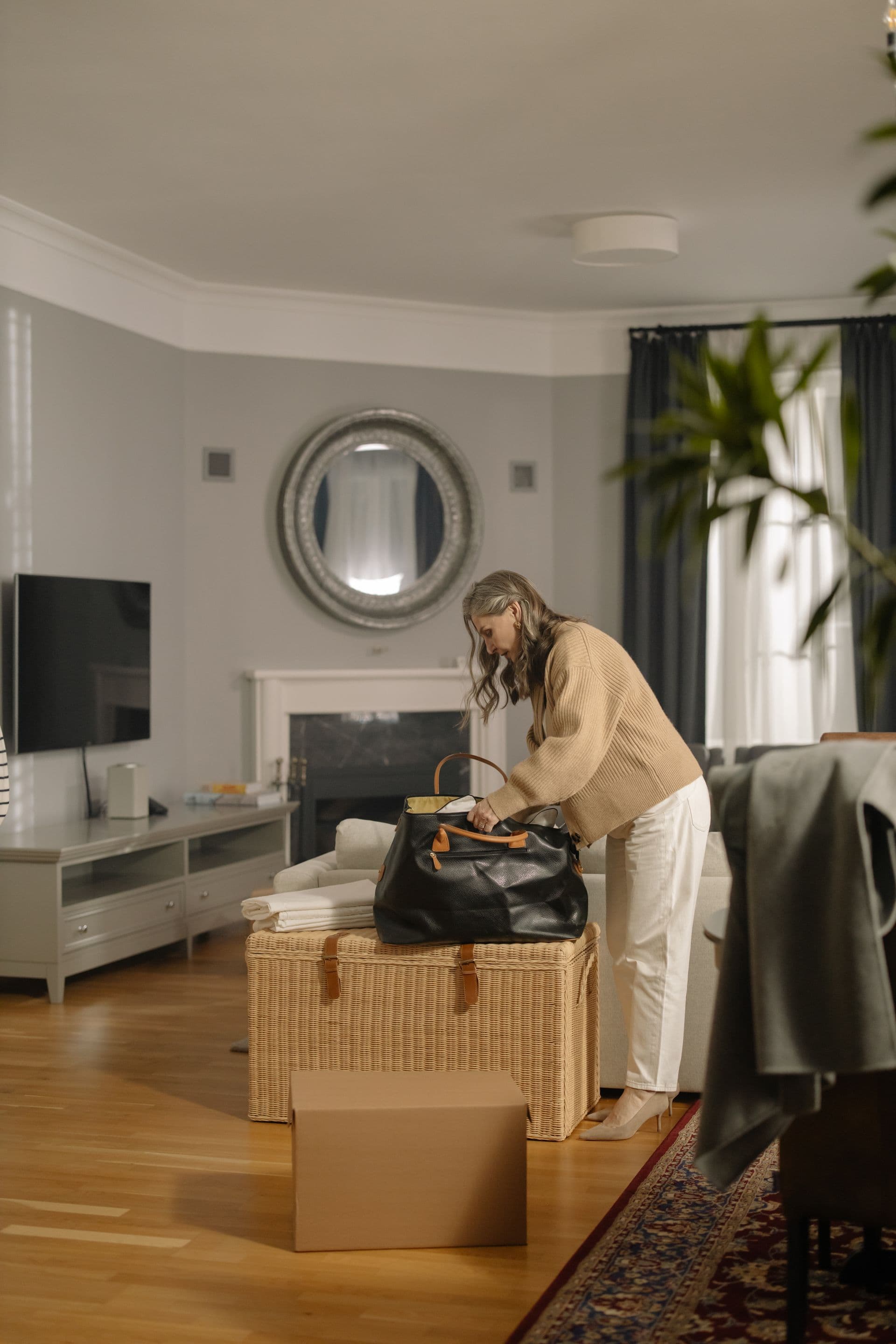 Ältere Dame packt in ihrem Wohnzimmer eine Tasche, daneben ein Weidenkorb und ein Umzugskarton